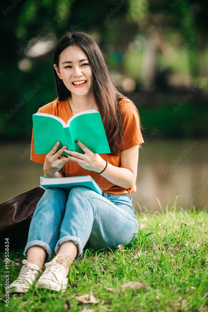 A young or teen asian girl student in university smiling and reading the book and look at the tablet