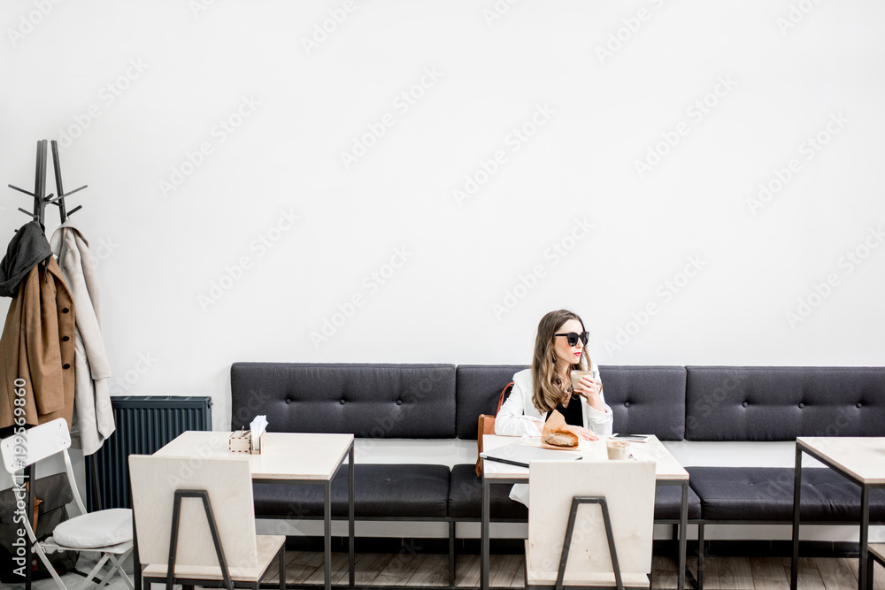 Stylish business woman in white jacket sitting during the coffee break in the modern cafe interior. 