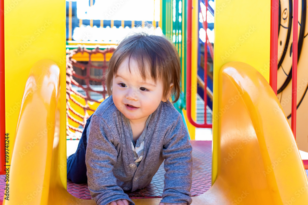 Mixed race toddler boy playing on a slide at a playground