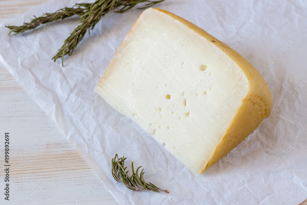 Greek cheese graviera on white wooden board with herbs.