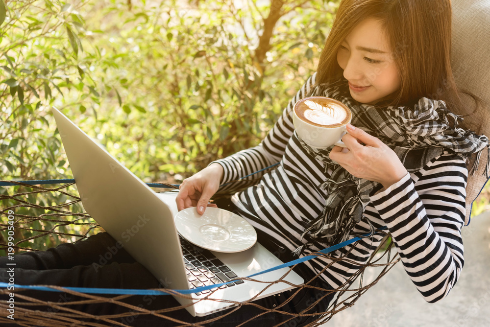 Young woman having coffee in hammock while use laptop, freelance life style conceptual, work anywher