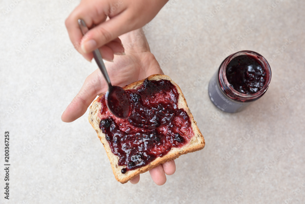 Blueberry jam with a spoon put on a piece of bread, which lies in the hand