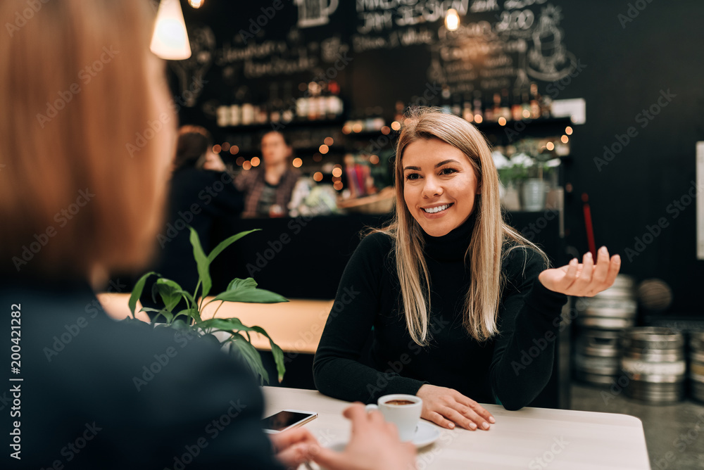 Front view of beautiful young woman talking to a friend at the cafe.