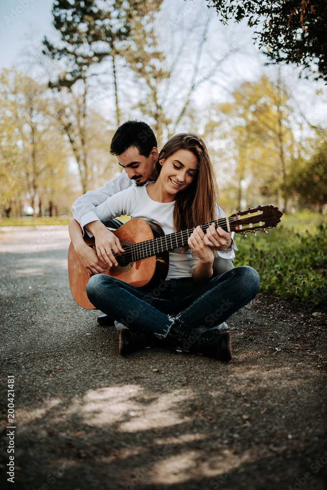 Young man teaching his girfriend guitar playing outdoors.