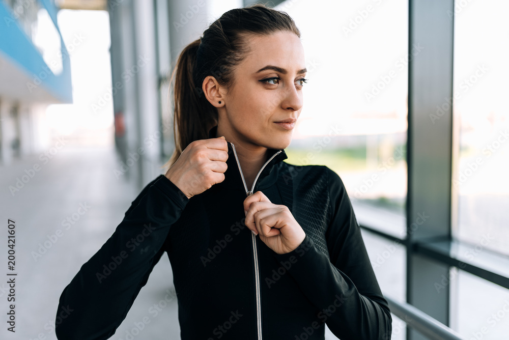 Girl taking off tracksuit jacket before workout. Close-up.