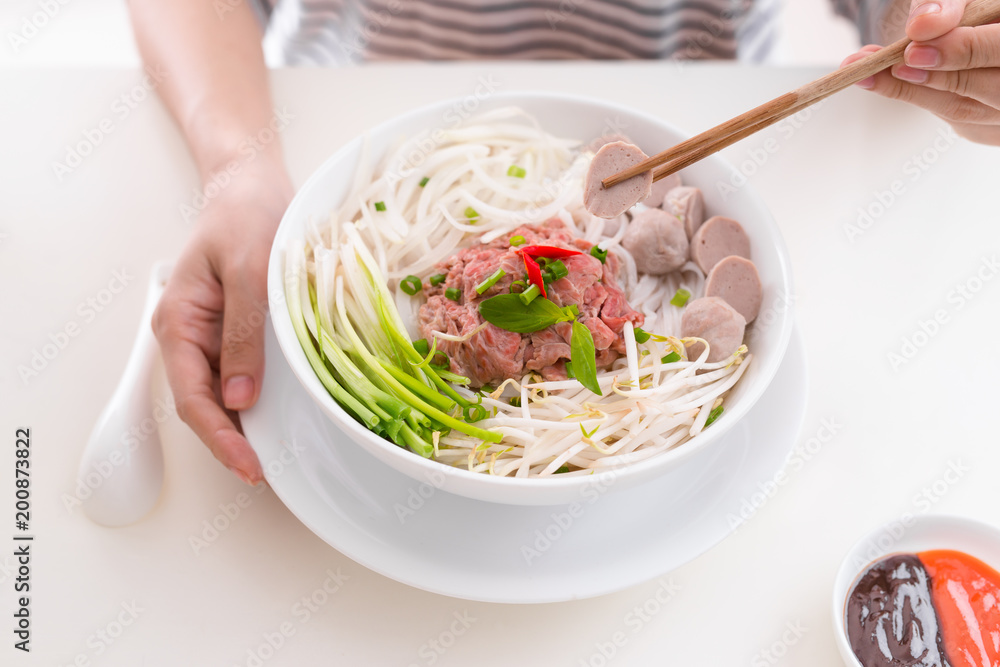 Woman eating traditional Vietnamese Pho noodle using chopsticks.