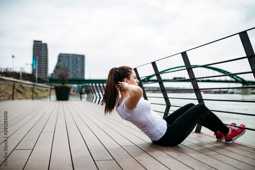 一个穿着运动服的女孩在码头上锻炼的侧视图，背景是城市和河流。