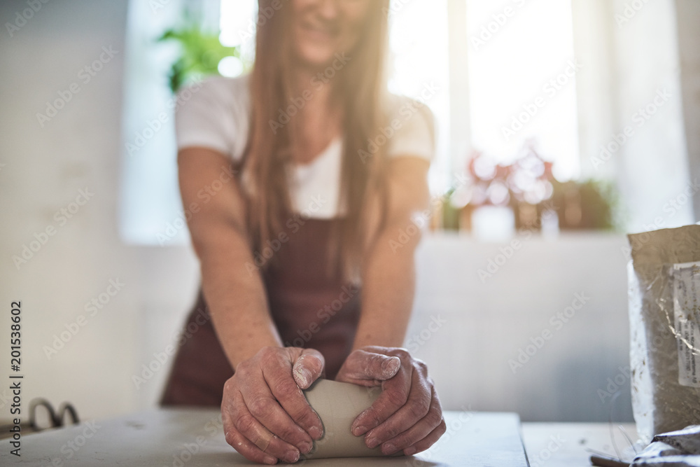 微笑的女性工匠在她的陶器工作室中塑造粘土