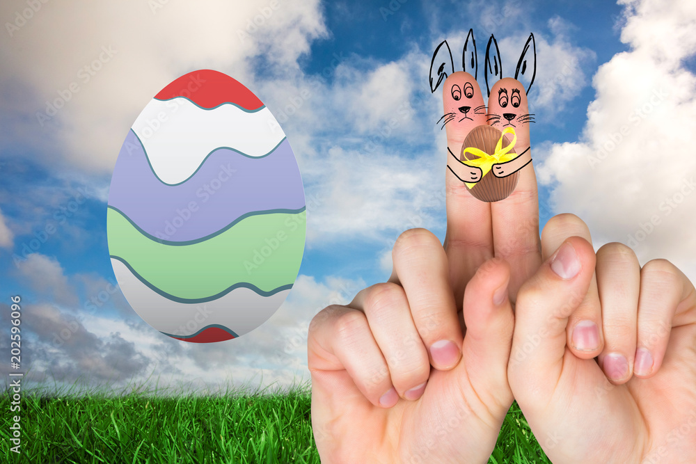 Fingers as easter bunny against green grass under blue sky