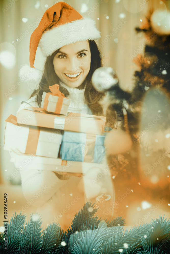 Festive brunette holding pile of gifts near a christmas tree against candle burning against festive 