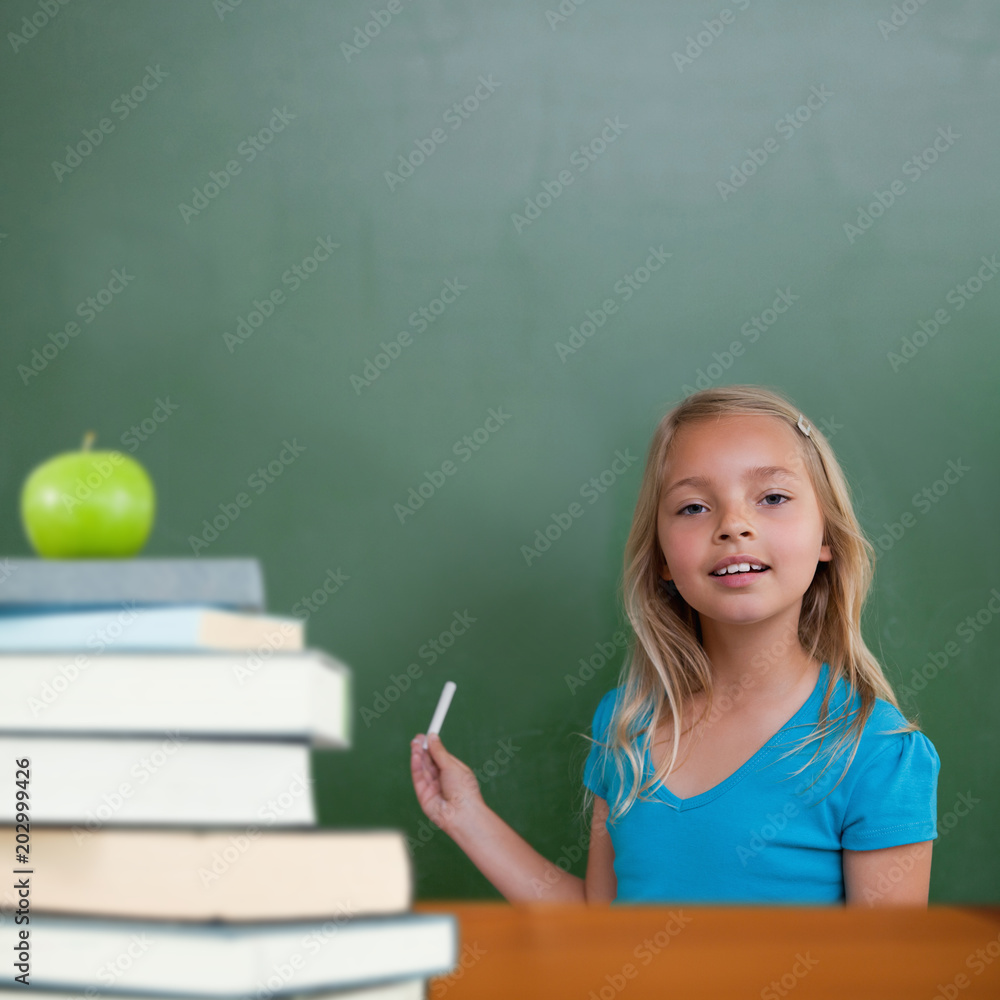 Green apple on pile of books against cute pupil holding chalk