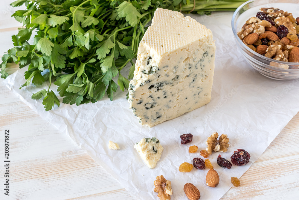 Tasty blue cheese with nuts and herbs on paper on white table