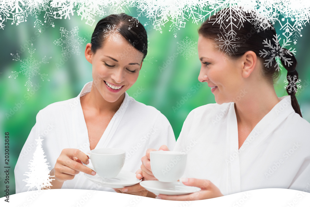 Beautiful friends in bathrobes drinking herbal tea against fir tree forest and snowflakes