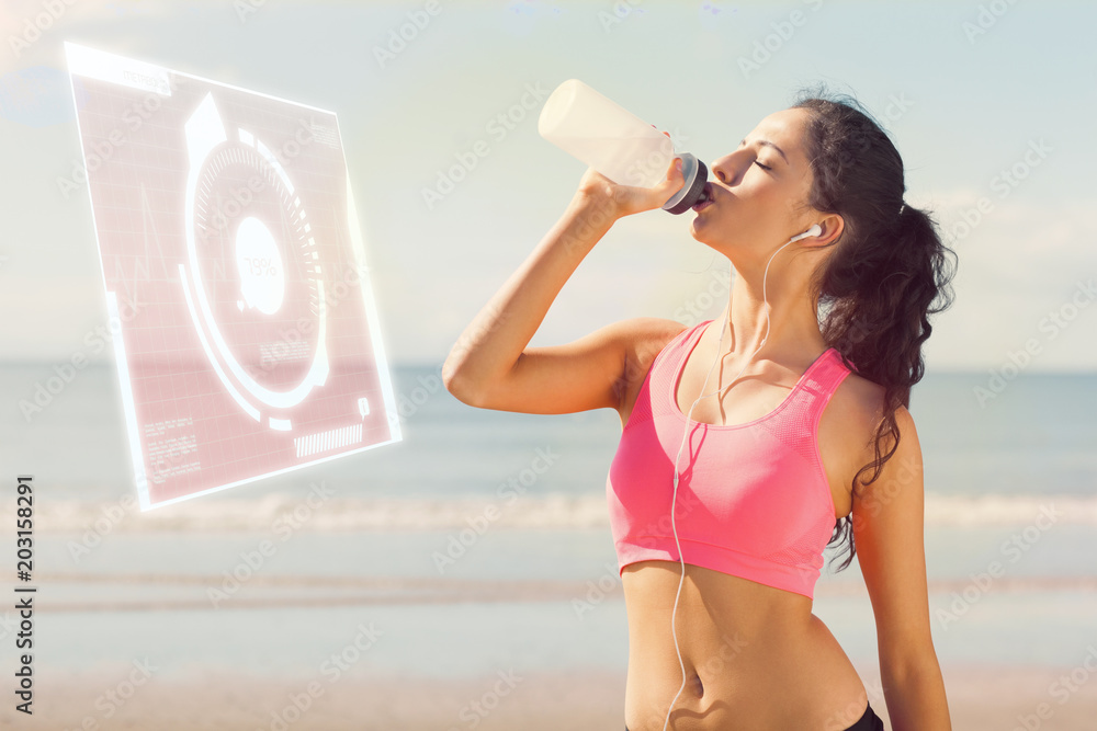 Beautiful healthy woman drinking water on beach against fitness interface