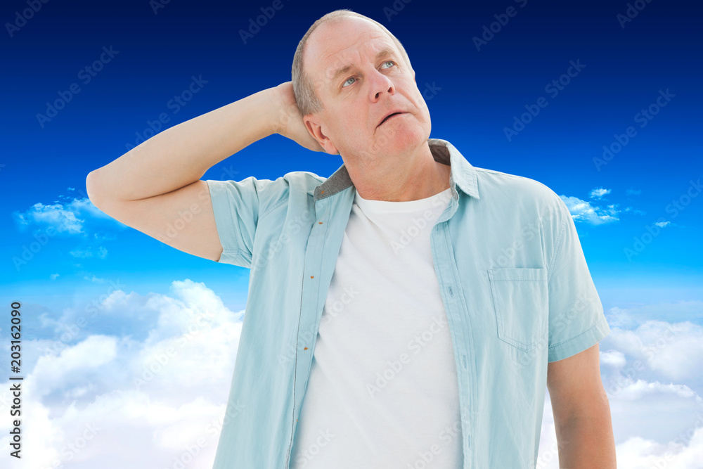 Thoughtful older man looking up against bright blue sky over clouds