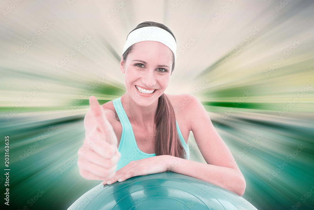 Smiling fit woman with fitness ball gesturing thumbs up against abstract background