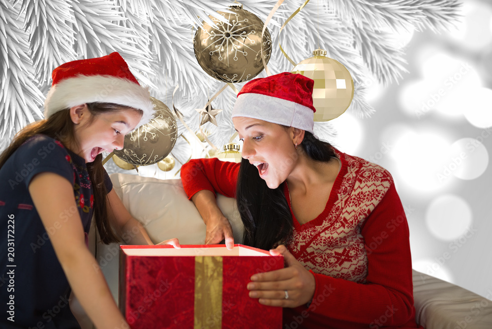 Mother and daughter opening gift against christmas decorations hanging from branch