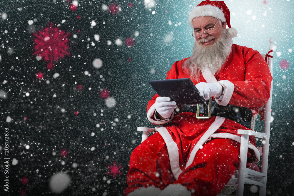 Cheerful Santa Claus using digital tablet against snow with red flakes