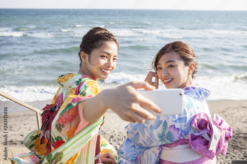 和服女性たちは海辺で写真を撮っている