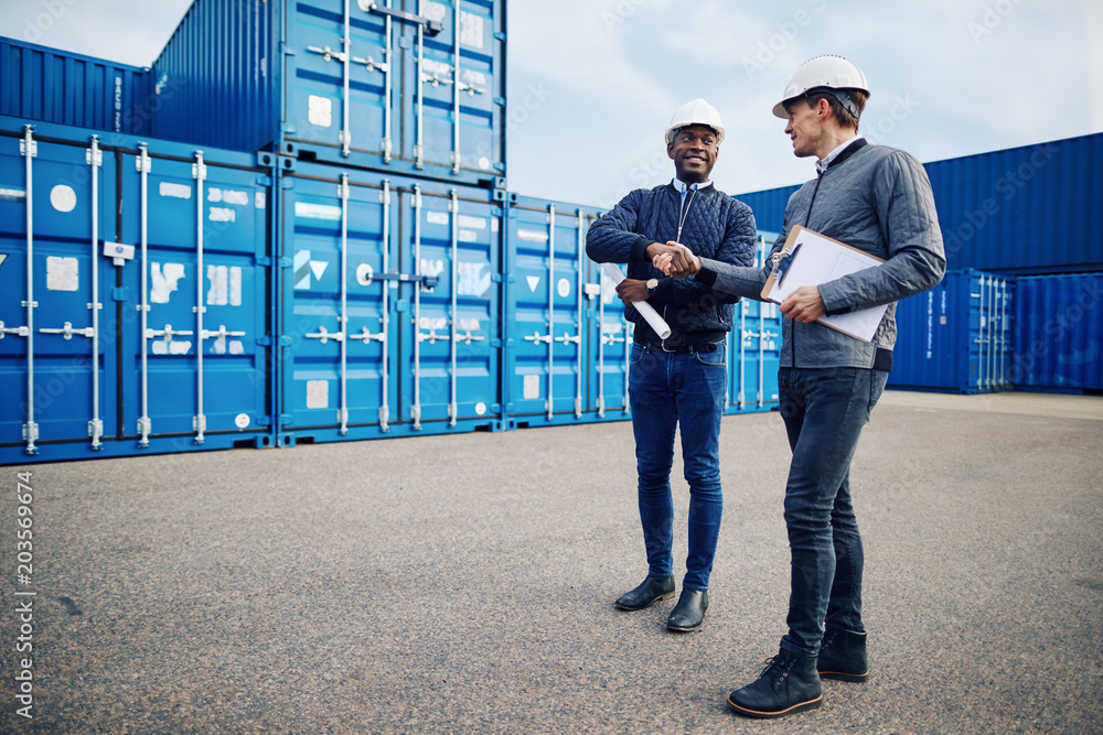 Smiling engineers shaking hands together in a shipping yard