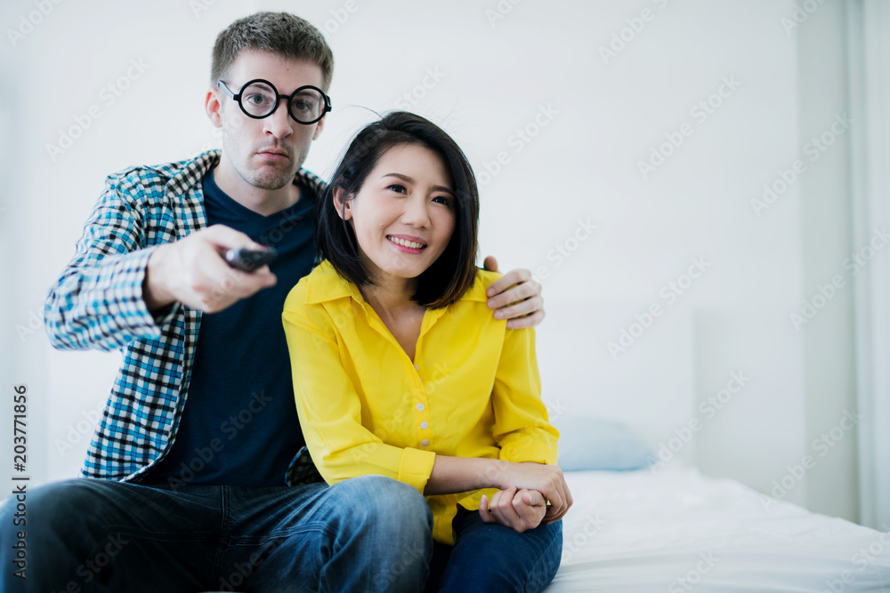 Happy smiling family couple caucasian husband and asian wife watching tv program on sofa in living r