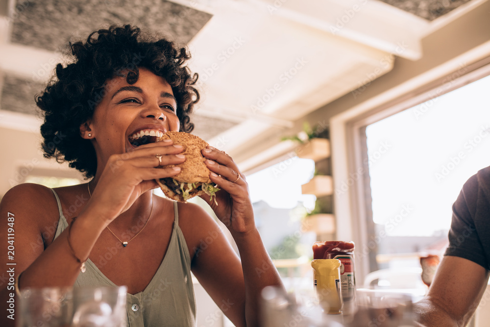 Woman enjoying eating burger at restaurant