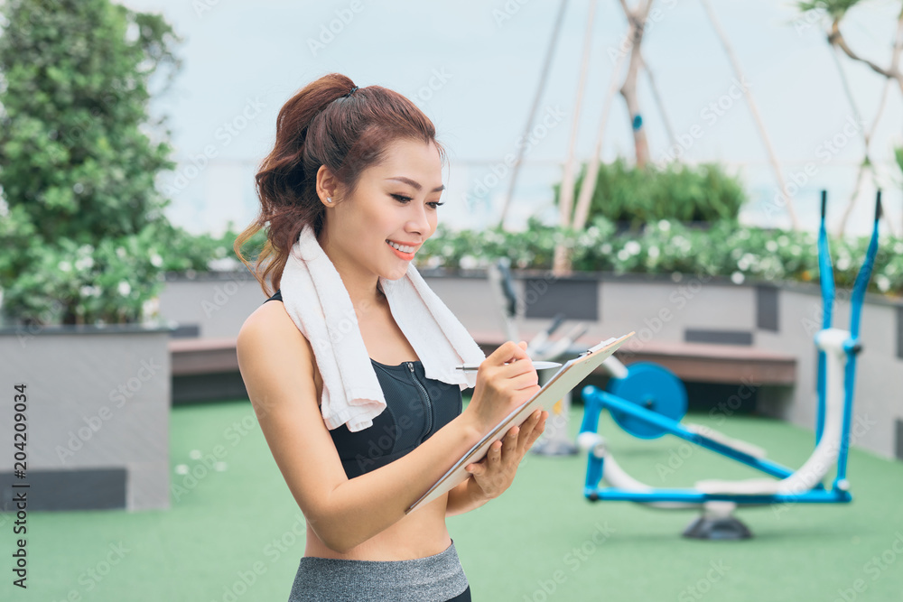 年轻的亚洲女教练在户外做笔记