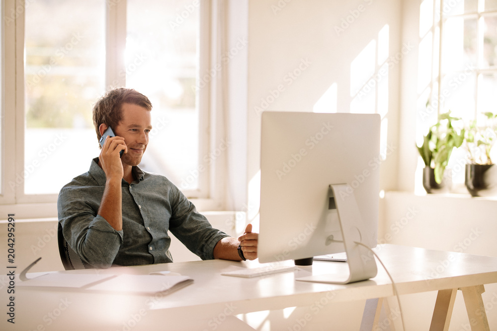 Entrepreneur talking on mobile phone while working on computer a