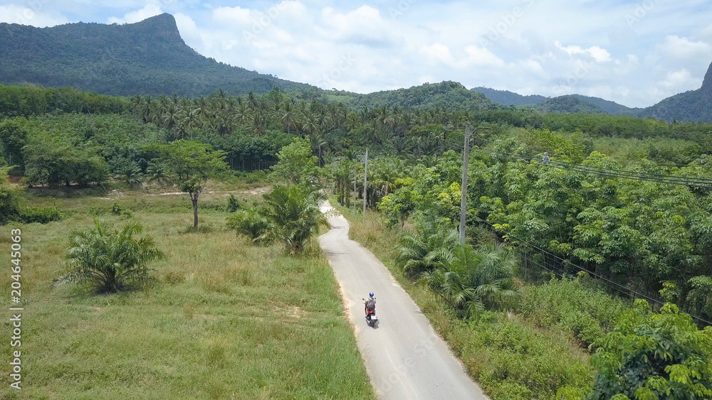 AERIAL: Flying behind female explorer riding her motorcycle into tropical jungle