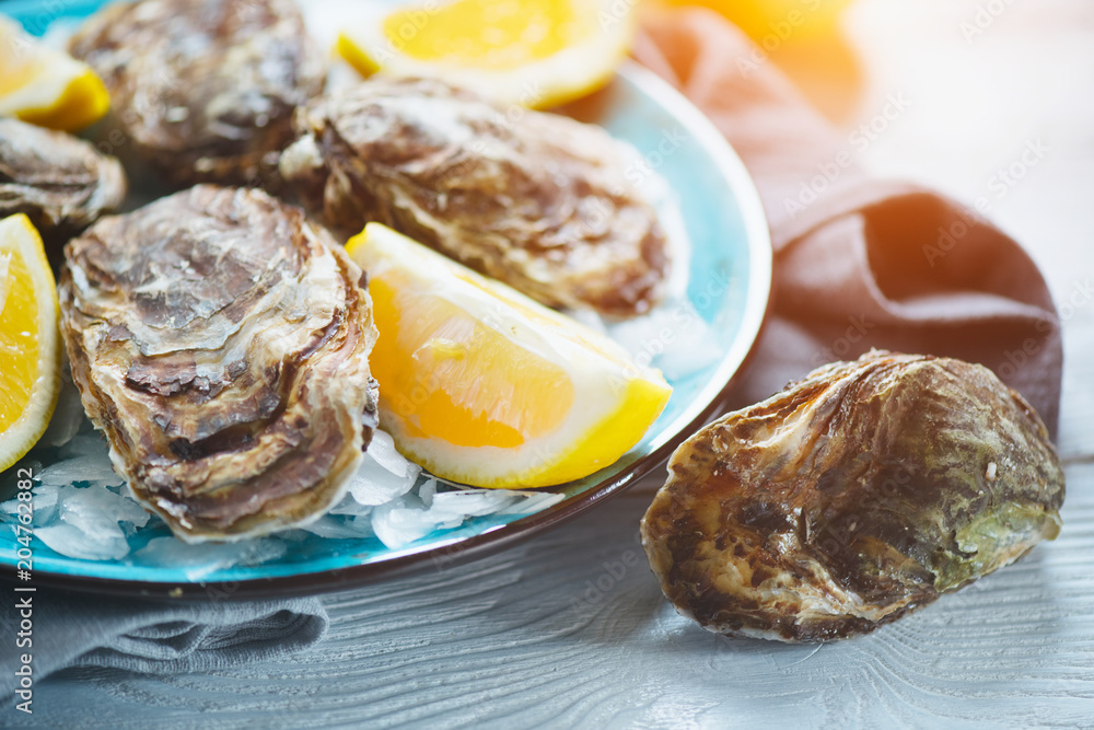 Fresh oysters close-up on blue plate, served table with oysters, lemon in restaurant. Gourmet food