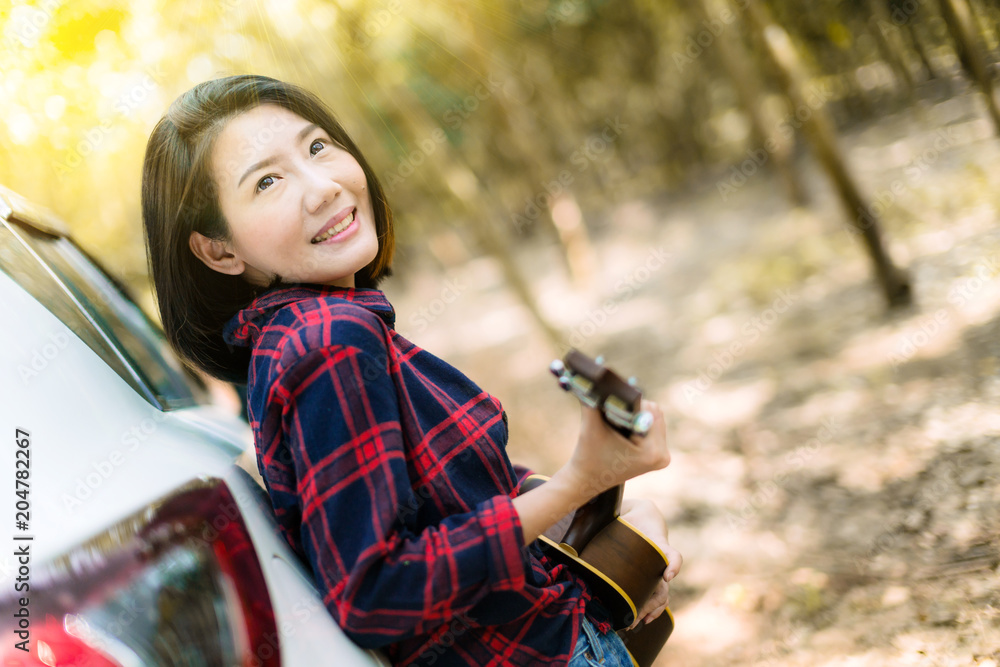 美丽的旅行亚洲女人享受在露营森林背景下玩尤克里里琴的快乐和快乐