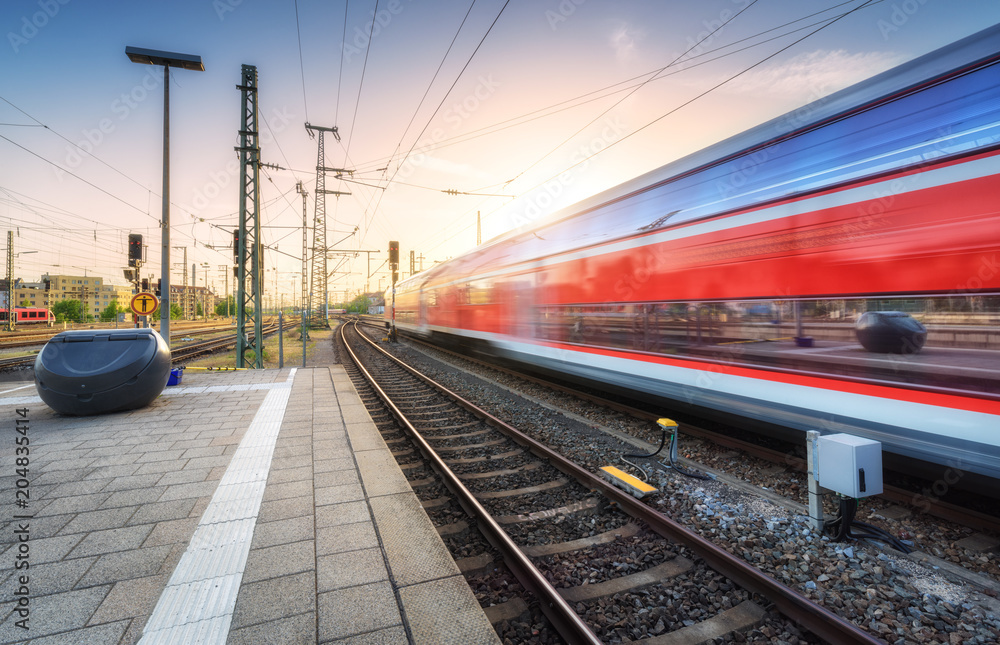 Red high speed train in motion on the railway station at colorful sunset. Germany. Blurred modern in