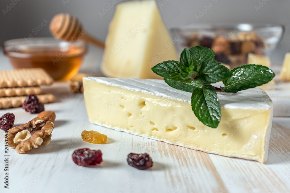 Fresh Brie cheese, Greek cheese graviera and a slice on white wooden board with nuts, honey and herb