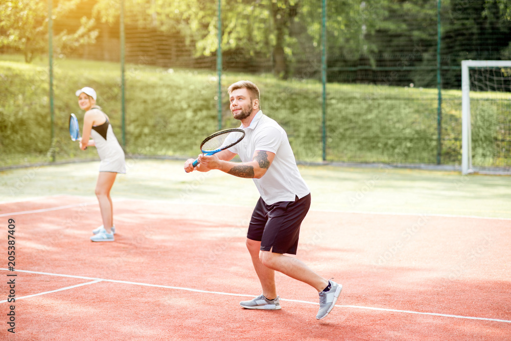 Young couple in white sports wear playing tennis on the tennis court outdoors