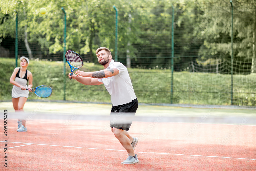 Young couple in white sports wear playing tennis on the tennis court outdoors