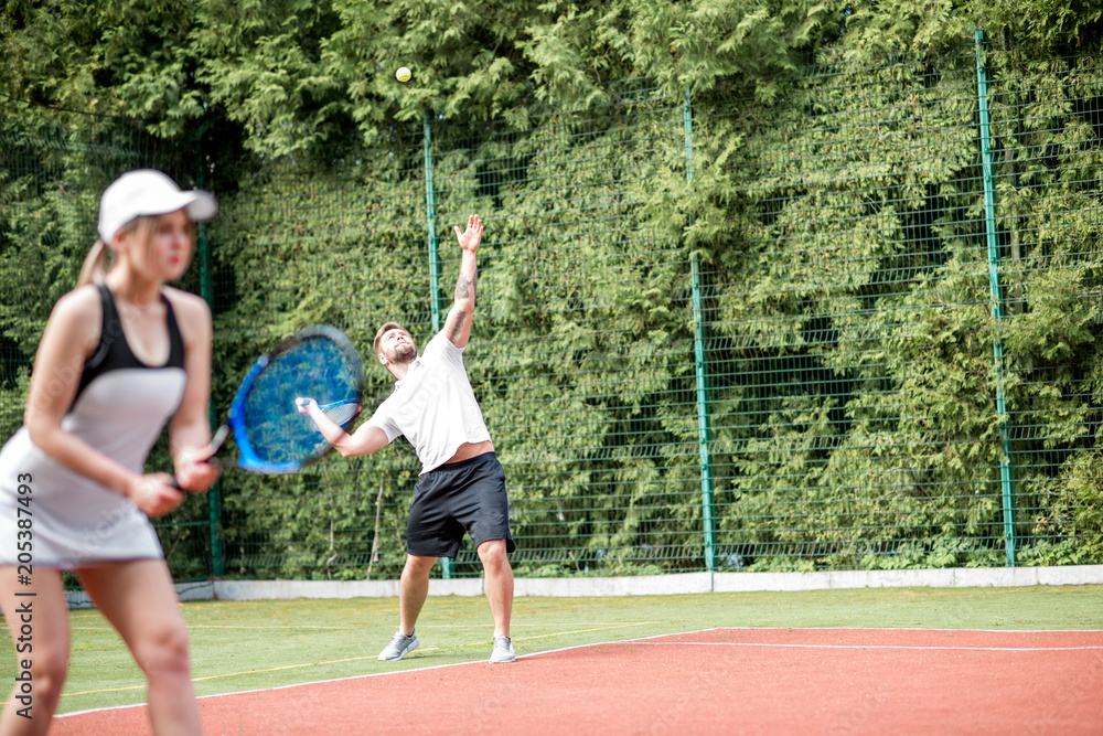 Young couple in white sports wear playing tennis on the tennis court outdoors