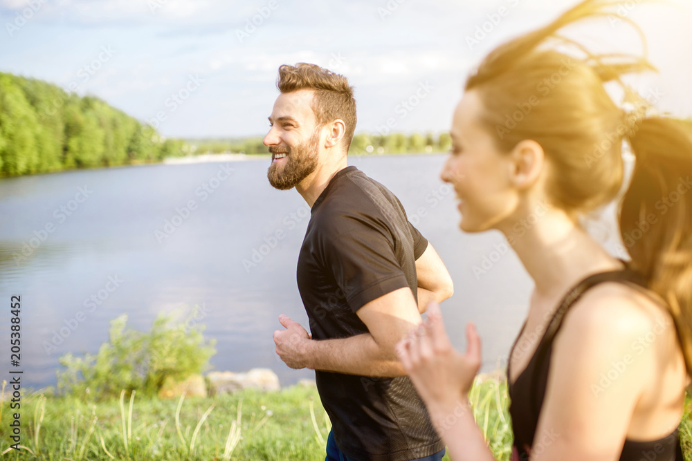 Couple in black sportswear running near the lake during the morning exercise