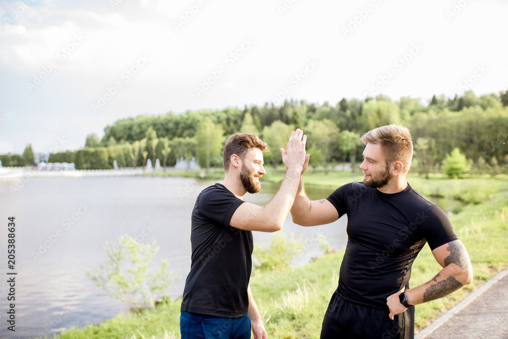 Male friends giving five after the sports training outdoors near the lake