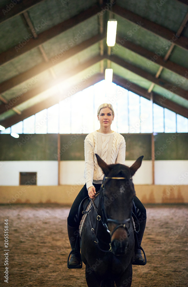 Blonde?confident female sitting astride dark horse