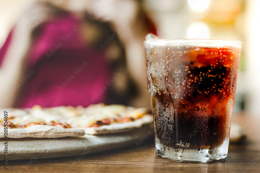 Closeup cola or soft drink. The cold cola in a glass with ice cube on the wooden table in pizzeria. 