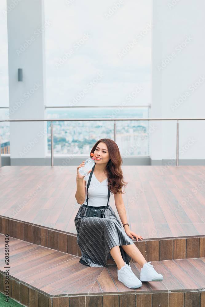 Adult woman relaxing sit on the sidewalk. Female enjoying her day.Holding a bottle of water, holding