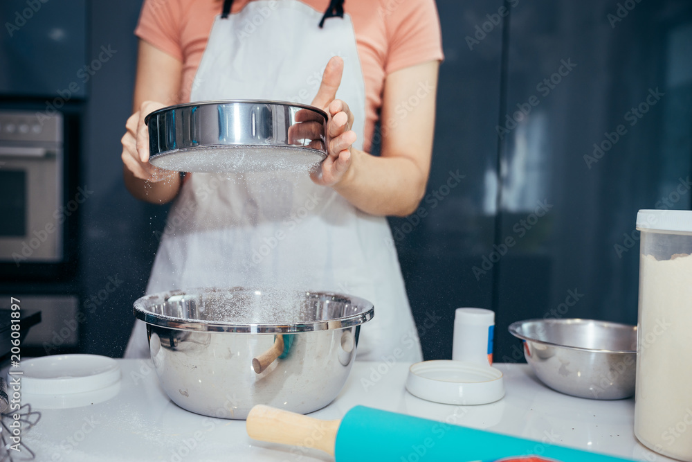 A woman sifting flour into a stainless bowl. Girl is sifting flour to making the bakery in her kitch