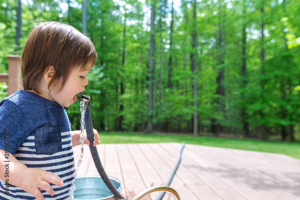 Young toddler boy playing with water from a garden hose outside