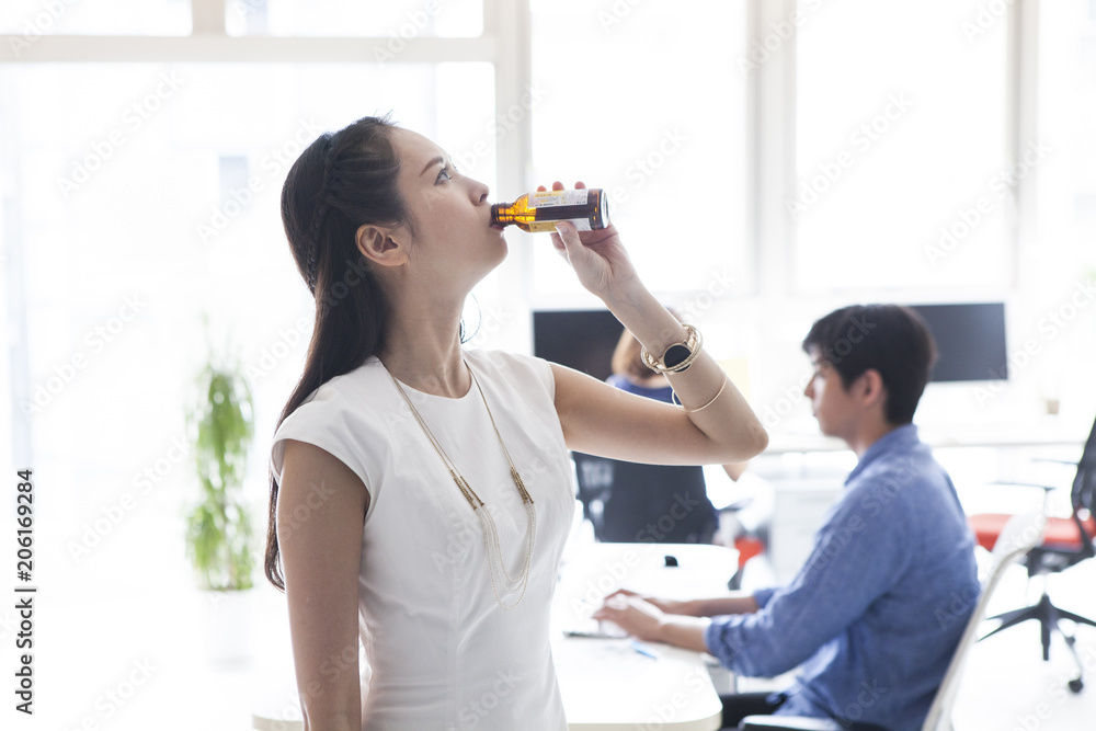 女性はオフィスで美容ドリンクを一気に飲んでいる