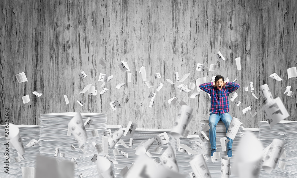 Attractive man sitting on pile of paper documents.