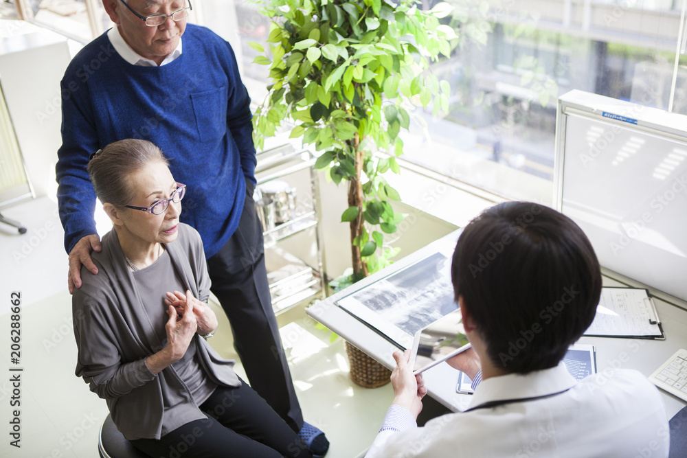 医者から診断結果を聞いている老女。夫が付き添っている。