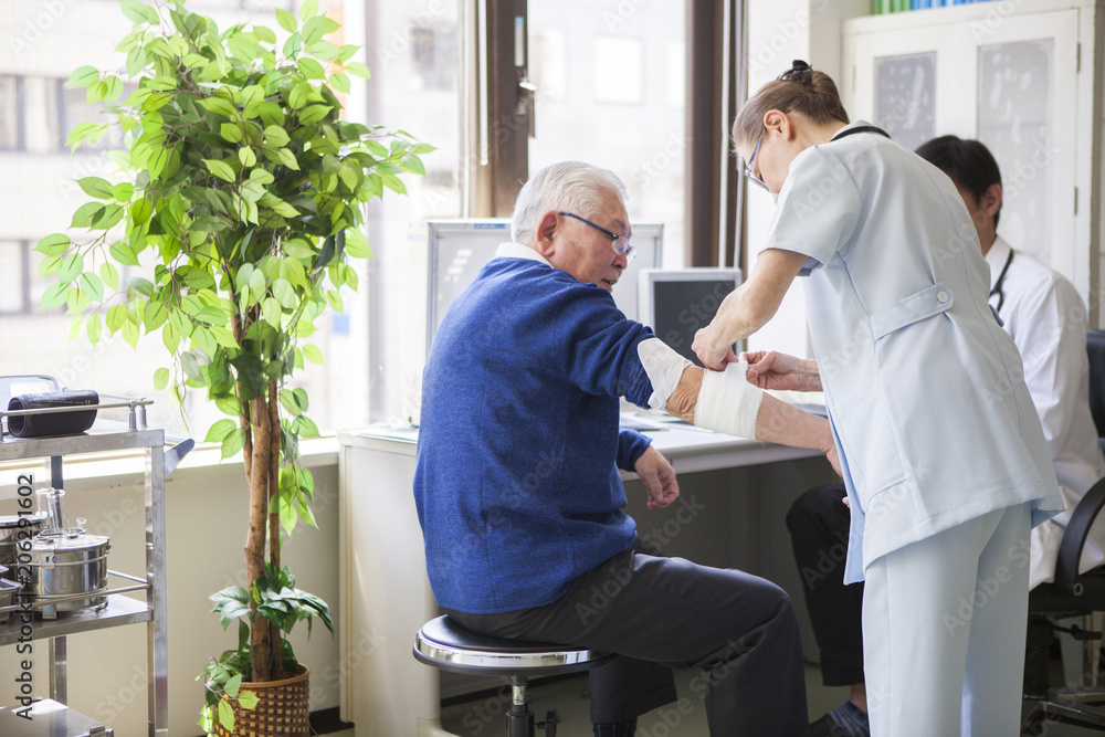 看護師が、医師の指示のもと、患者の老人の腕に包帯を巻いている。