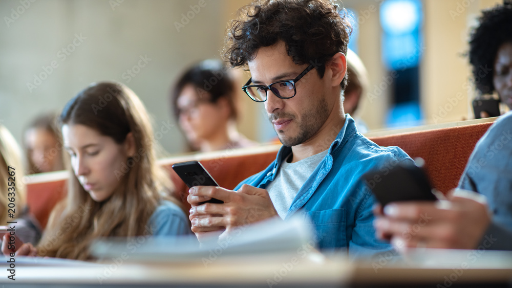 西班牙裔男子在课堂上演讲时使用智能手机。年轻聪明的学生学习