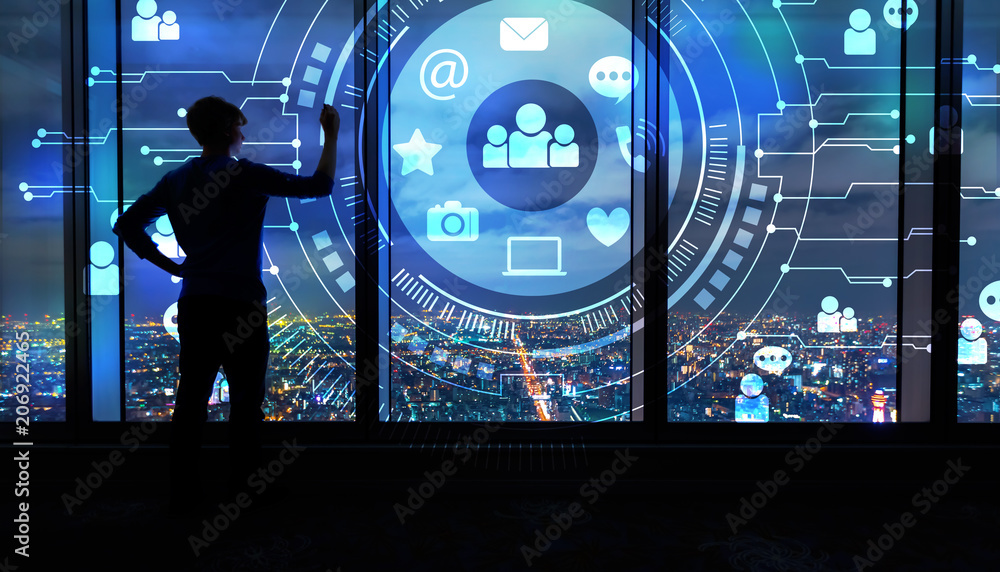 Social Media with man writing on large windows high above a sprawling city at night