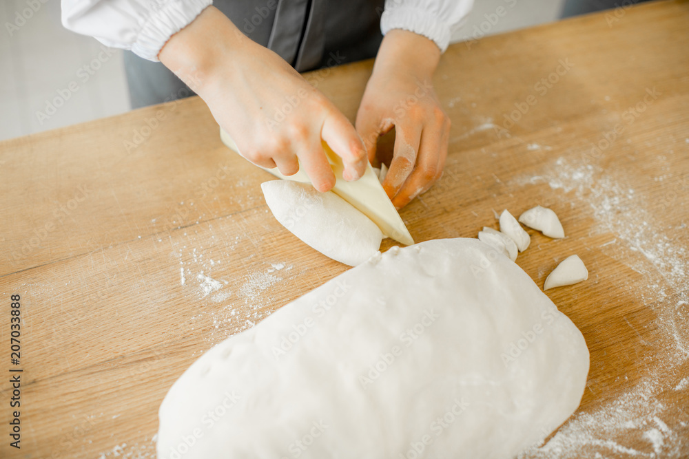 Baker forming daugh with hands for baking on the wooden table at the manufacturing